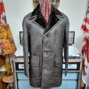 May include: A brown leather jacket with a fur collar and four button closures. The jacket has two pockets on the front and a long, fitted style.
