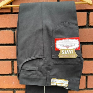 Peut inclure: Pantalon noir à jambe droite avec une étiquette Levi's Sta-Prest. L'étiquette porte le texte "STA-PREST LEVI'S PANTS WITH THE FAMOUS STRAIGHT LEG" et la taille "27 34".