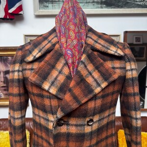 May include: A vintage double-breasted plaid coat in shades of orange, brown, and black. The coat features a classic notched collar and dark buttons. A paisley scarf in red, blue, and yellow is draped over the coat's shoulders.