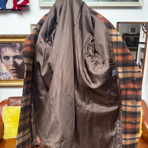 May include: A vintage plaid coat in shades of brown and orange, displayed open to reveal a brown satin lining. The coat is on a mannequin, showcasing its interior construction and design. The coat has a classic, timeless style.