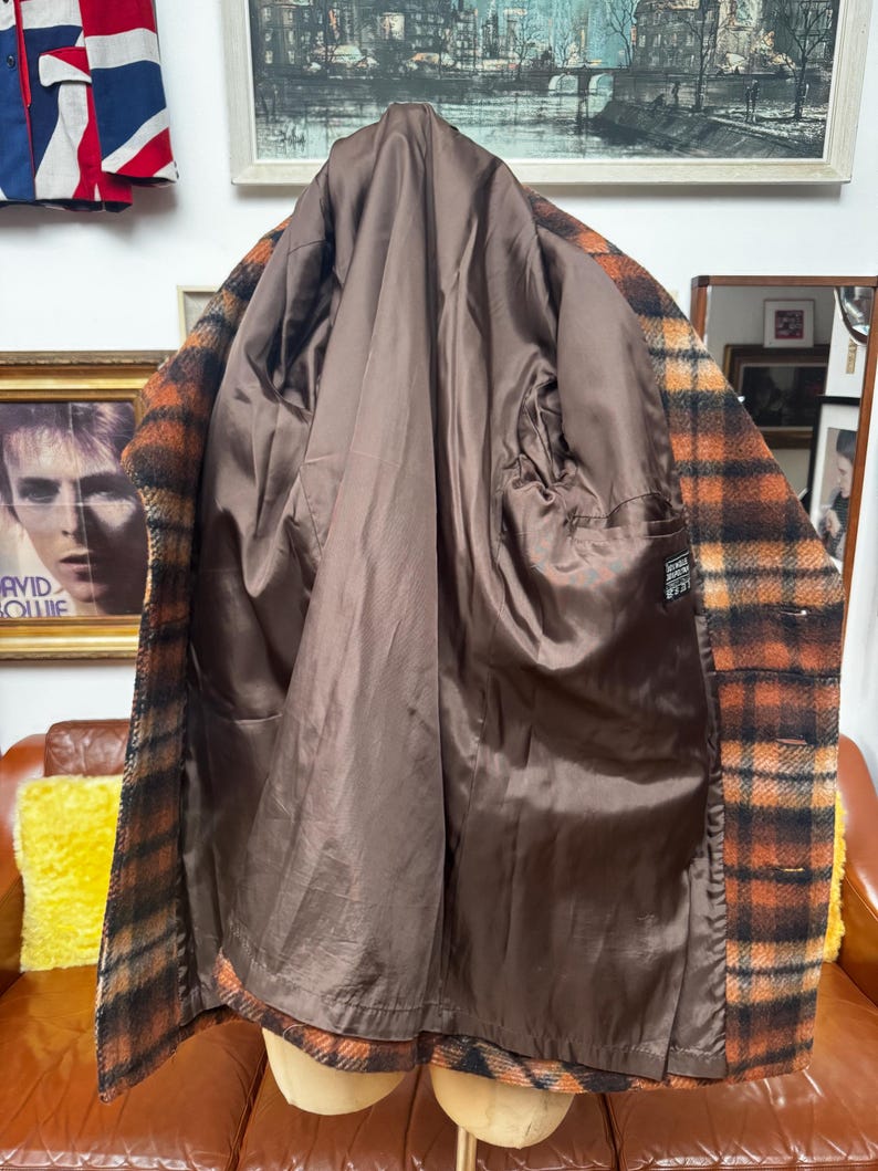May include: A vintage plaid coat in shades of brown and orange, displayed open to reveal a brown satin lining. The coat is on a mannequin, showcasing its interior construction and design. The coat has a classic, timeless style.