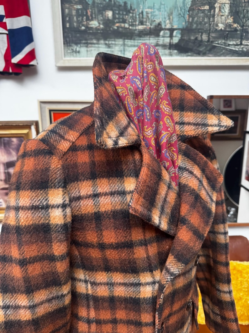 May include: A vintage plaid coat in shades of brown and orange with a wide collar. A paisley scarf in red, purple, and yellow is draped over the collar. The coat has a classic, tailored design, suggesting a retro style.