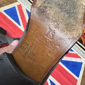 K&ouml;nnte beinhalten: Nahaufnahme der Sohle eines schwarzen Lederschuhs. Die braune Sohle tr&auml;gt den Markennamen "ISTONY" und Gr&ouml;&szlig;enangaben. Der Schuh weist Gebrauchsspuren auf. Im Hintergrund eine Union Jack Flagge.