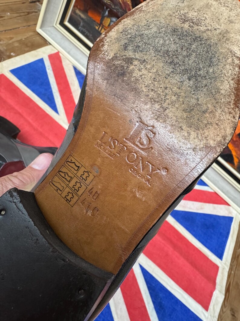 K&ouml;nnte beinhalten: Nahaufnahme der Sohle eines schwarzen Lederschuhs. Die braune Sohle tr&auml;gt den Markennamen "ISTONY" und Gr&ouml;&szlig;enangaben. Der Schuh weist Gebrauchsspuren auf. Im Hintergrund eine Union Jack Flagge.