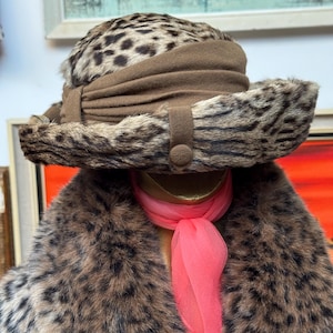 May include: A vintage leopard print hat with a brown band and button detail. The hat is paired with a matching leopard print faux fur coat and a bright pink scarf. The ensemble evokes a classic, retro aesthetic.