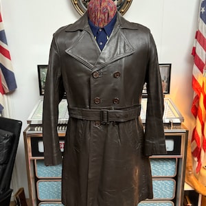 May include: A brown leather trench coat with a double breasted closure, a belt, and long sleeves.