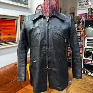 May include: A black leather jacket with a zip-up front, collar, and multiple pockets. The jacket is displayed on a mannequin. A colorful scarf is draped around the mannequin's neck.