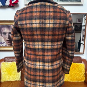 May include: A brown, orange, and black plaid jacket. The jacket is displayed on a mannequin. The jacket has a collared neckline and long sleeves. The jacket is made of a textured fabric.