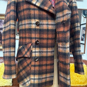 May include: A vintage plaid coat in shades of brown, orange, and black. The coat features a double-breasted design with three buttons, a notched collar, and two front pockets. The coat's interior lining is visible, showcasing a paisley pattern.