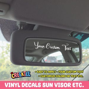 Könnte beinhalten: Eine schwarze Sonnenblende mit dem weißen Text "Your Custom Text". Das Bild enthält auch den Text "EASY TO APPLY - YOUR CUSTOM TEXT + CUSTOMIZE COLORS OR TEXT ETC." und "VINYL DECALS SUN VISOR ETC."