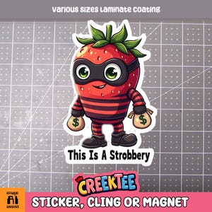 May include: A red and black cartoon strawberry character wearing a black mask and holding two bags of money. The text "This Is A Strobbery" is below the character. The text "CREEKTEE" is below the text. The text "STICKER, CLING OR MAGNET" is below the text.