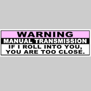 以下が含まれることがあります： ピンクのストライプがついた白い警告ステッカー。ステッカーには「WARNING MANUAL TRANSMISSION IF I ROLL INTO YOU, YOU ARE TOO CLOSE.」と書いてあります。