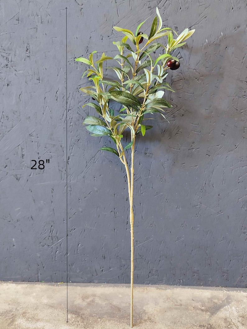May include: A 28-inch artificial olive branch with green leaves and black olives. The branch is on a gray background.