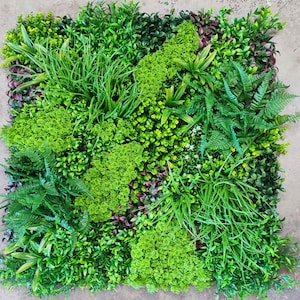May include: A square artificial plant panel featuring a variety of green foliage, including ferns, grasses, and small flowering plants. The panel has a mix of light and dark green leaves, with some burgundy accents, creating a textured, natural look.