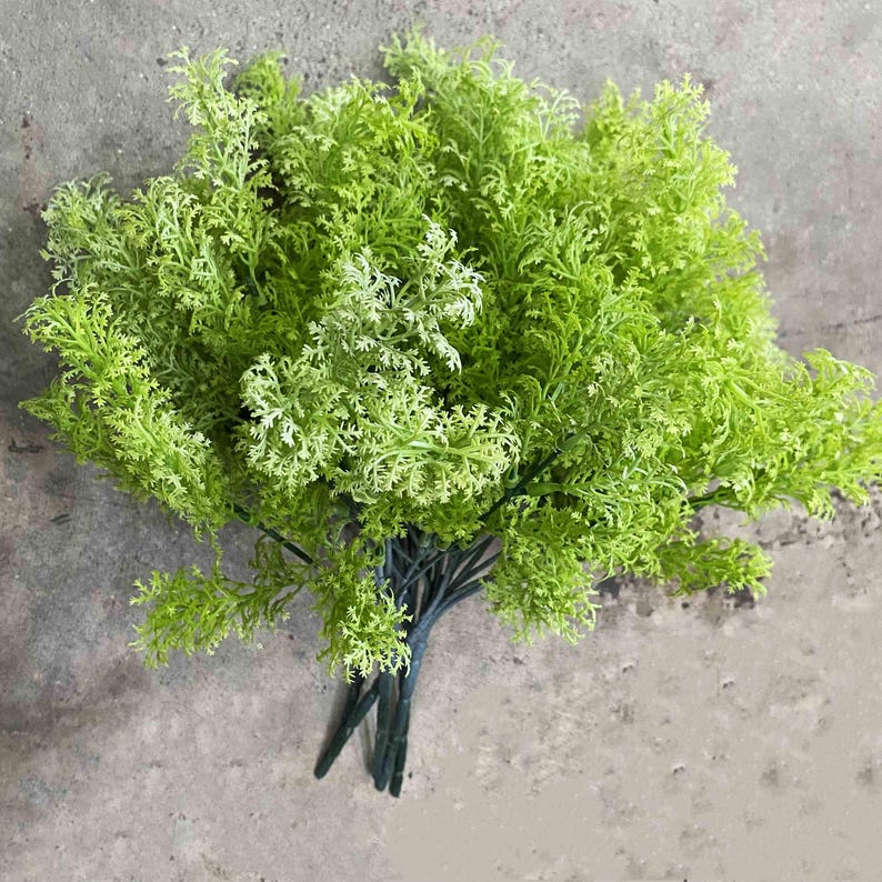 May include: A bunch of artificial green fern sprigs with a feathery texture. The stems are bundled together and ready to be used in a floral arrangement.