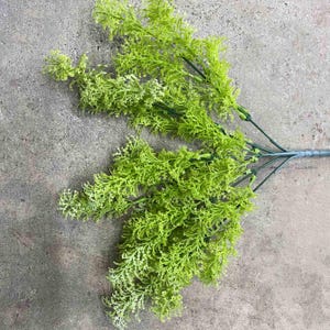 May include: A bunch of artificial green leafy sprigs with a wire stem. The sprigs are arranged in a fan shape.
