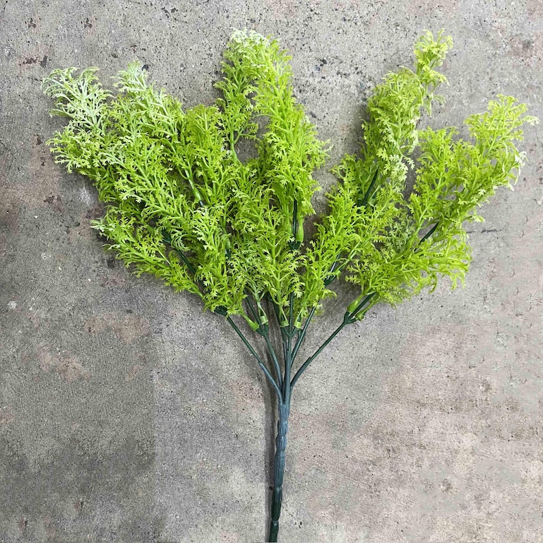 May include: A bunch of artificial green leafy sprigs with a long stem. The sprigs are arranged in a bouquet shape.