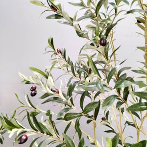 May include: A close-up of an artificial olive tree with green leaves and dark purple olives. The tree is in a pot, but the pot is not visible in the image.