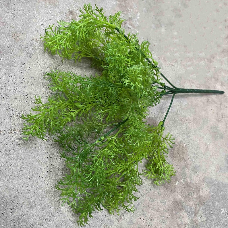 May include: A bunch of artificial green fern sprigs with a wire stem. The sprigs are arranged in a fan shape and have a delicate, feathery texture.