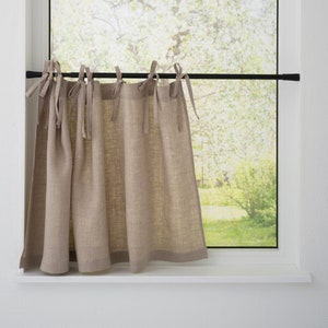 May include: A window with a white frame and a view of a tree with green leaves. A beige linen curtain hangs from a black rod, tied with matching fabric ties. The curtain is gathered and hangs down to the windowsill.