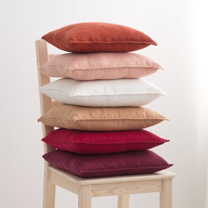 A stack of decorative square pillow cases in shades of orange pink and red on chair.
