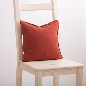 Burnt orange decorative square pillow case on a chair.