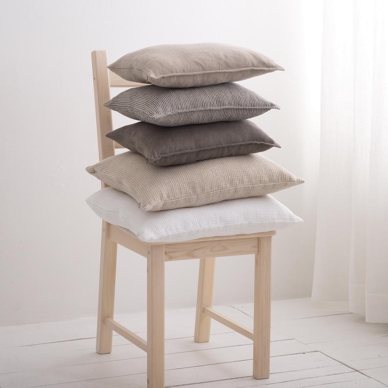Puede incluir: Una silla de madera con una pila de cinco almohadas en varios tonos de beige y marr&oacute;n. Las almohadas est&aacute;n dispuestas en forma de pir&aacute;mide, con la almohada m&aacute;s grande en la parte inferior y la m&aacute;s peque&ntilde;a en la parte superior.