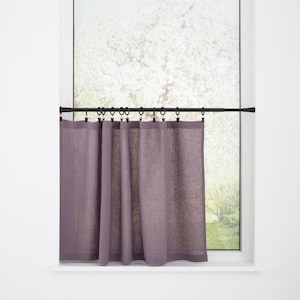 May include: A window with a white frame and a view of a tree. A black curtain rod holds a set of purple linen curtains. The curtains are hung with black rings and are partially covering the window.