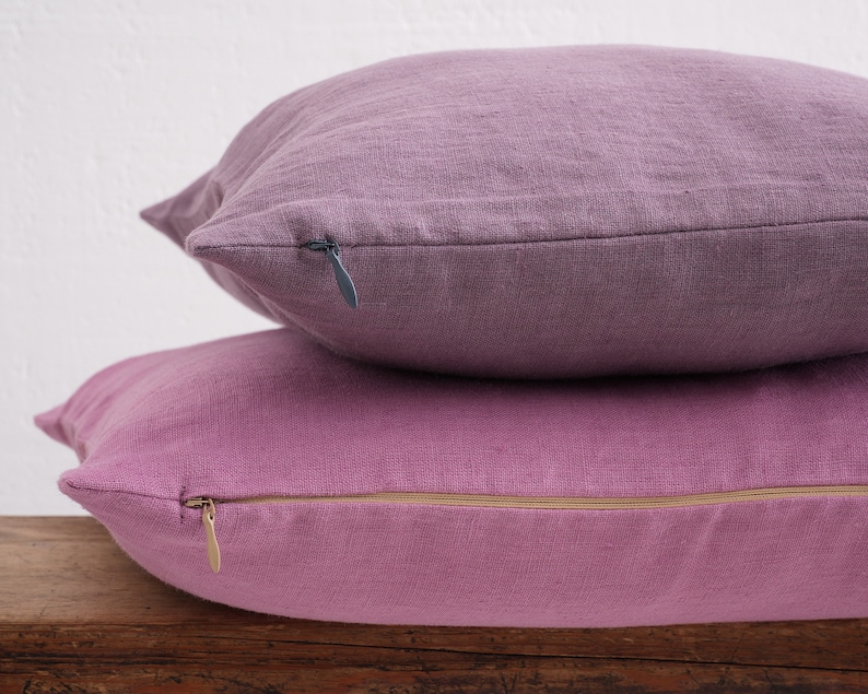 Stacked deocorative square pillow covers, in the colors dusty purple and pink with a hidden zipper closure.
