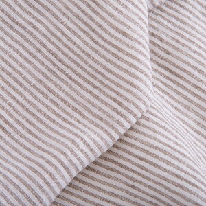 May include: Close-up of a white and brown striped fabric with a diagonal fold. The fabric has a linen texture.