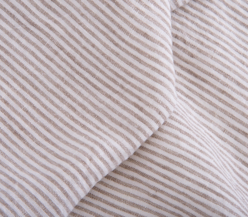 May include: Close-up of a white and brown striped fabric with a diagonal fold. The fabric has a linen texture.