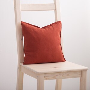 May include: A burnt orange linen throw pillow on a light wood chair.