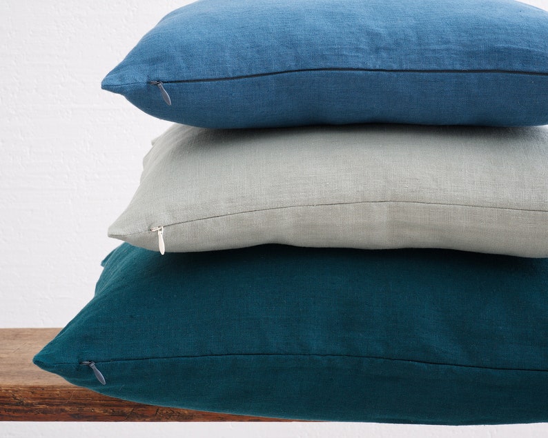 Stacked deocorative square pillow covers, in the colors denim blue, mint and dark teal with a hidden zipper closure.