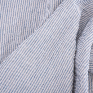 May include: Close-up of a blue and white striped fabric with a textured linen look. The fabric is folded and the stripes are diagonal.