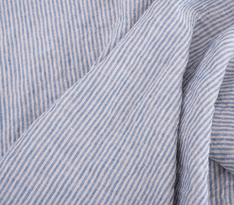 May include: Close-up of a blue and white striped fabric with a textured linen look. The fabric is folded and the stripes are diagonal.