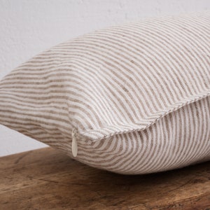 Striped white square pillow case with a hidden zipper closure on a wooden bench.