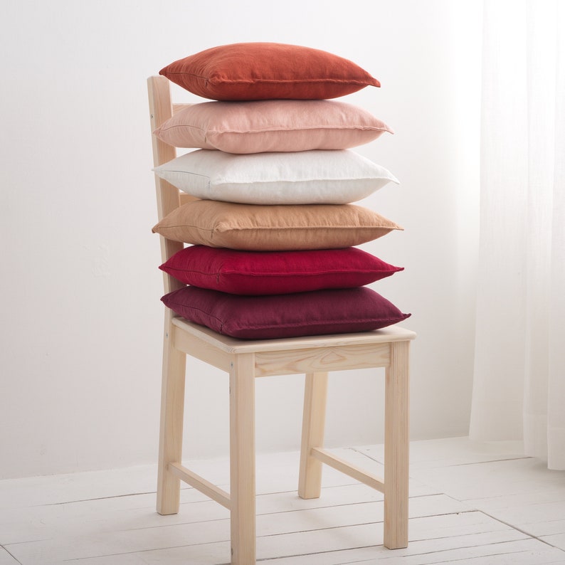 A stack of decorative square pillow cases in shades of orange pink and red on chair.