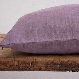 Close up of a dusty purple deocorative square pillow cover with a hidden zipper closure on a wooden bench.