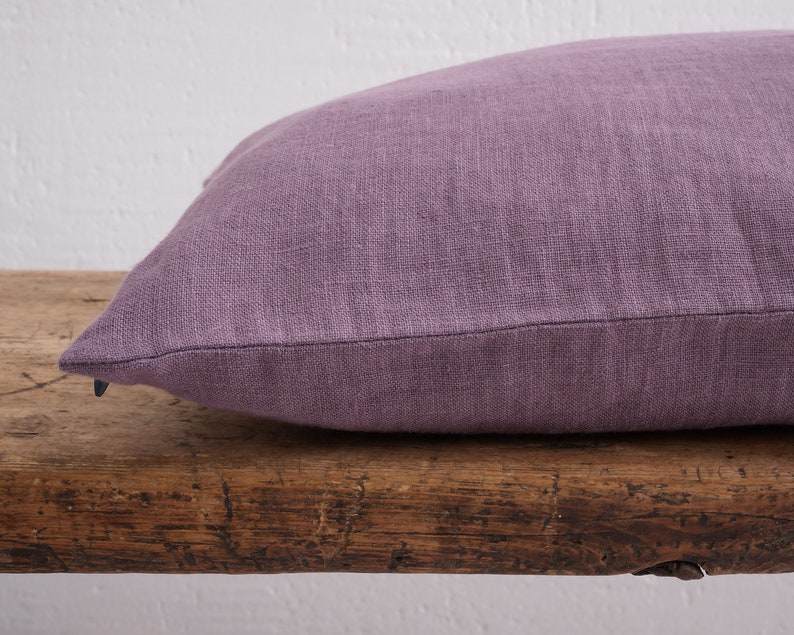 Close up of a dusty purple deocorative square pillow cover with a hidden zipper closure on a wooden bench.