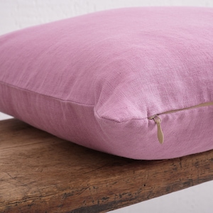 Close up of a pink deocorative square pillow cover with a hidden zipper closure on a wooden bench.