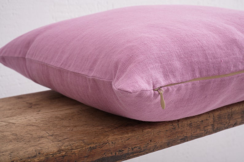 Close up of a pink deocorative square pillow cover with a hidden zipper closure on a wooden bench.