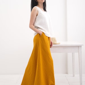 May include: A woman wearing a white sleeveless top and a long, mustard yellow linen skirt. The skirt has a wide, flowing silhouette.
