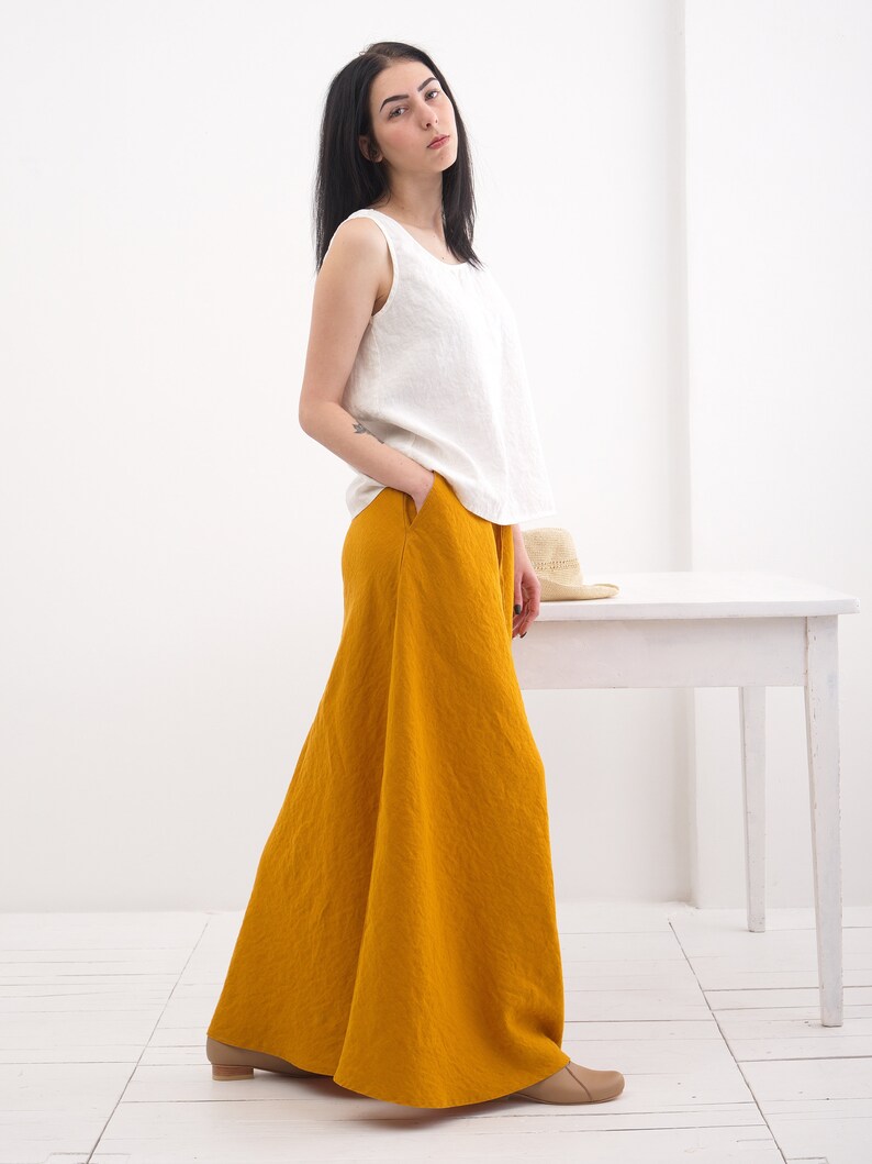 May include: A woman wearing a white sleeveless top and a long, mustard yellow linen skirt. The skirt has a wide, flowing silhouette.