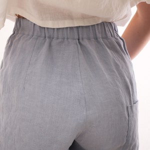 May include: Light blue linen shorts with an elastic waistband and side pockets. The shorts are made of a soft, breathable fabric, perfect for warm weather. The shorts are shown from the back.