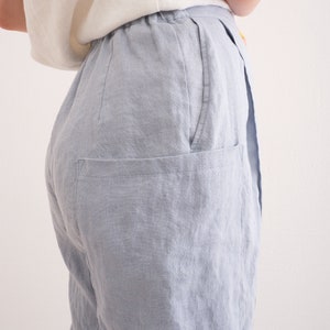 May include: Light blue linen pants with a relaxed fit. The pants feature a high waist, a visible pocket, and a soft, textured appearance. The fabric appears to be lightweight and breathable, suitable for warm weather.