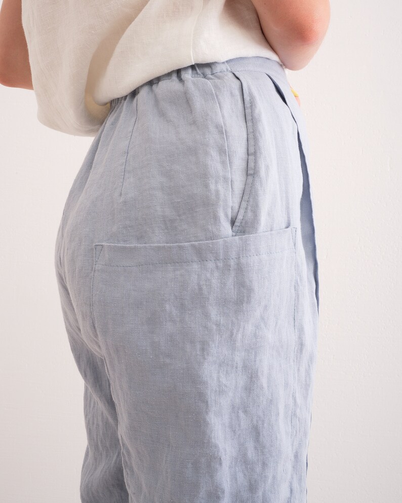 May include: Light blue linen pants with a relaxed fit. The pants feature a high waist, a visible pocket, and a soft, textured appearance. The fabric appears to be lightweight and breathable, suitable for warm weather.