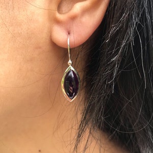 May include: A pair of silver earrings with a dark purple gemstone in a marquise shape.