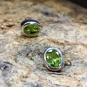 May include: A pair of silver stud earrings with oval-shaped green gemstones.