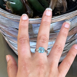 May include: A silver ring with a large, square-shaped, light blue gemstone.