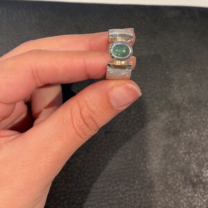 Op de afbeelding: Een zilveren ring met een groene edelsteen in een getextureerde band.